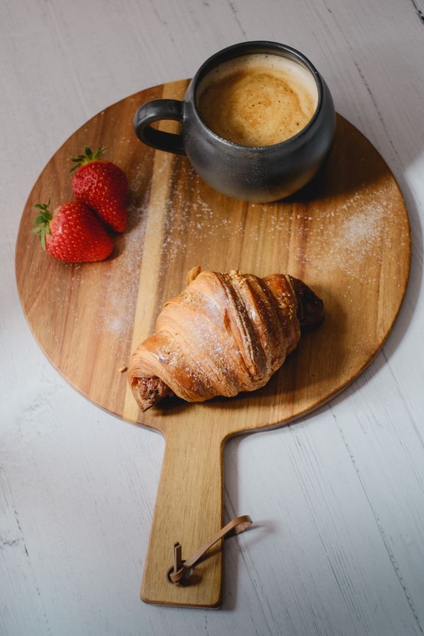 Serving board with a cup of coffee, a croissant and strawberry.
