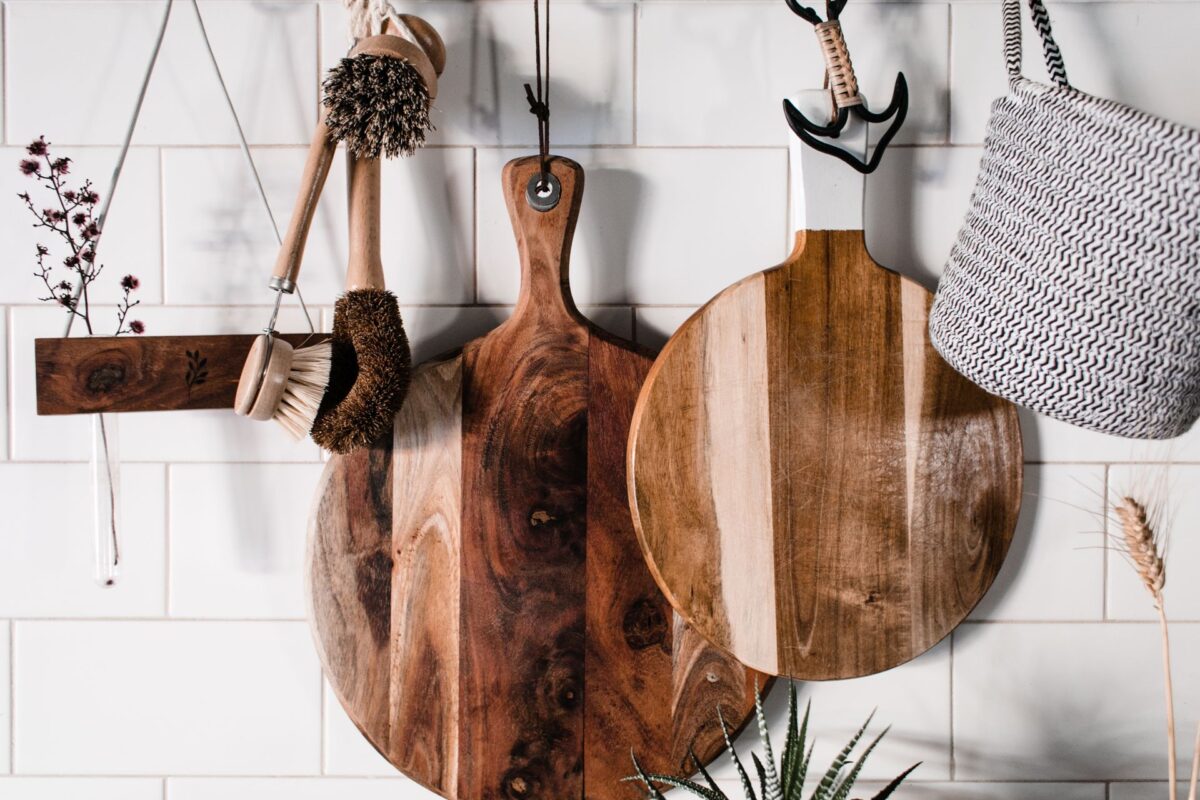 Wooden cutting boards and cleaning brushes hanging on a tiled kitchen wall.
