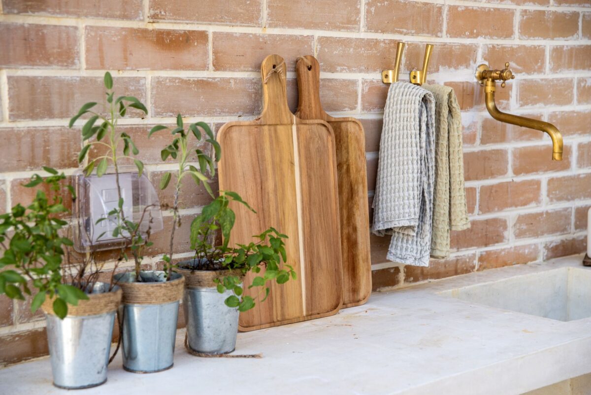 Two wooden cutting boards leaning against a brick wall beside a kitchen sink.